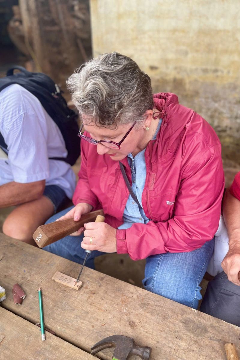 A guest learning traditional wood carving techniques from a master artisan, preserving Vietnam’s ancestral crafts