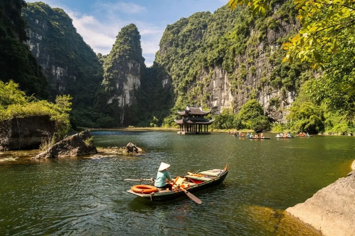 Rowboats and a waterside pavilion beneath limestone cliffs in Trang An, Ninh Binh
