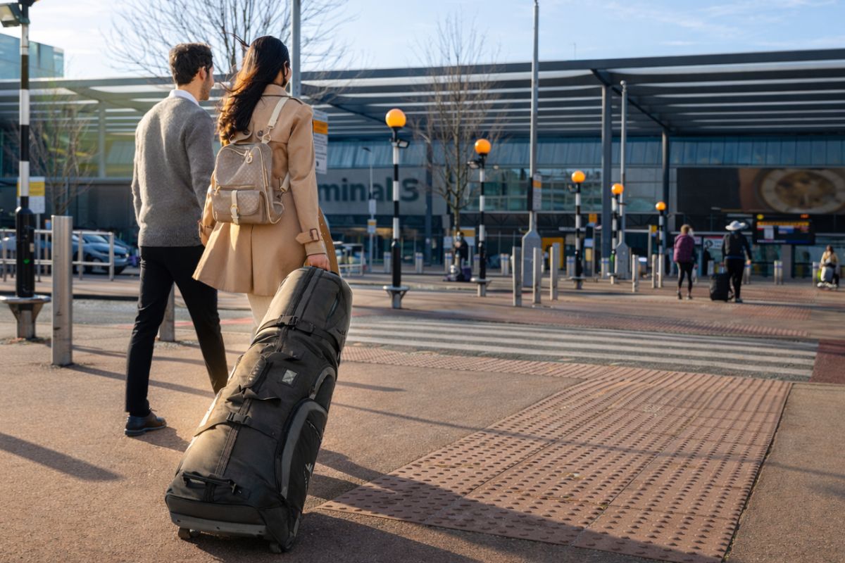Travellers walking towards an airport terminal with a wheeled golf travel bag