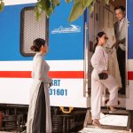 vietnam luxury train boarding scene, attendant assisting elegant passenger at carriage door beside blue-white carriage