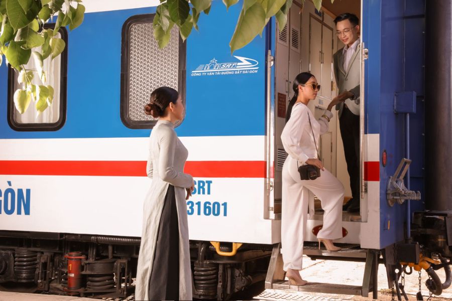 vietnam luxury train boarding scene, attendant assisting elegant passenger at carriage door beside blue-white carriage